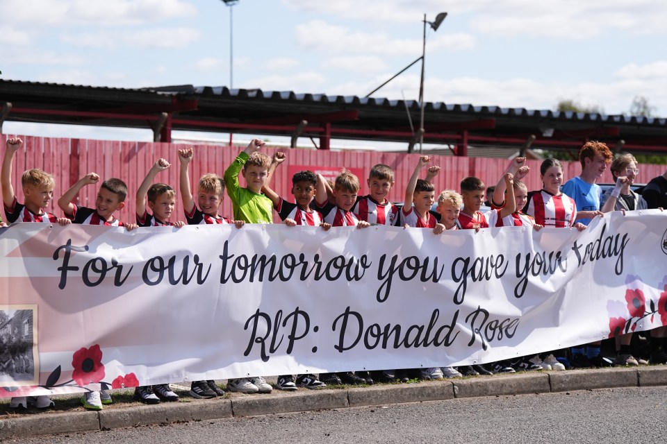 Youth football players holding a banner that reads "For our tomorrow you gave your today. RIP: Donald Rose".
