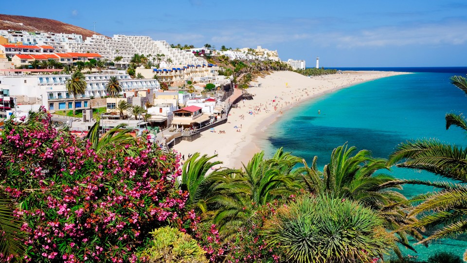 Playa de Morro Jable beach in Fuerteventura, Canary Islands, with hotels, lighthouse, and palm trees.