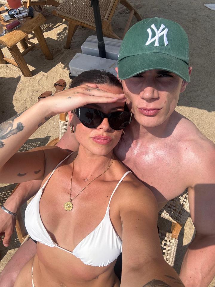 Selfie of a couple on a beach; the woman is wearing a white bikini top.