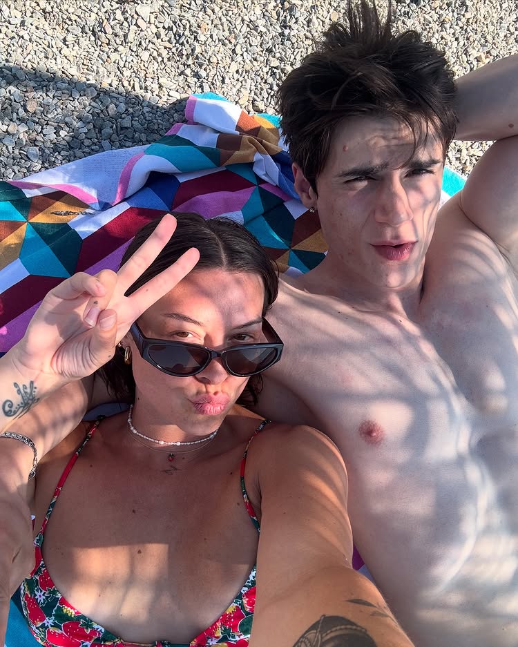 A couple lying on a beach towel, taking a selfie.