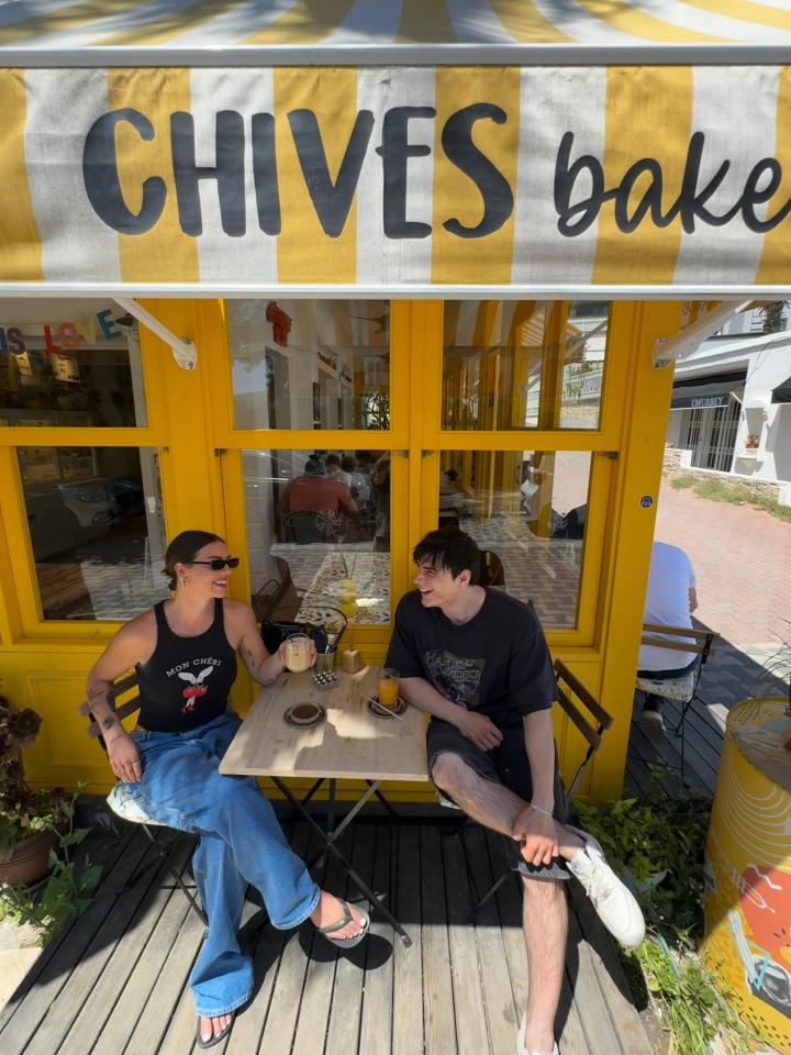 A couple sits at a small table outside a yellow cafe, enjoying drinks.