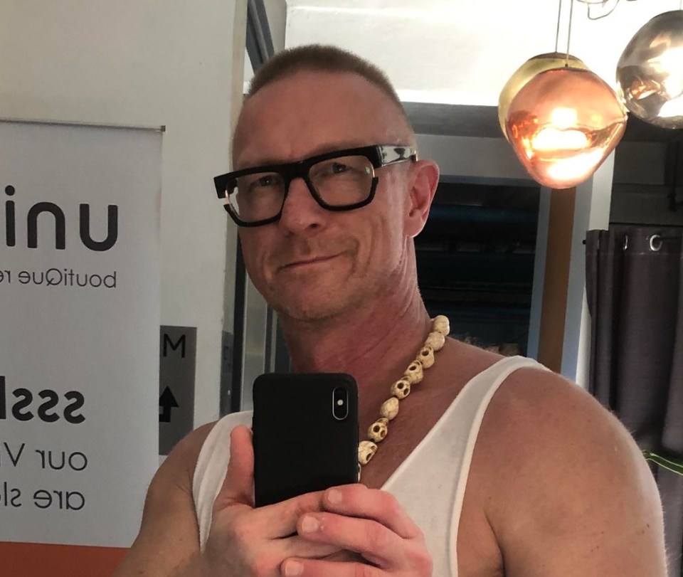 Selfie of a man holding a phone, wearing glasses and a skull necklace.