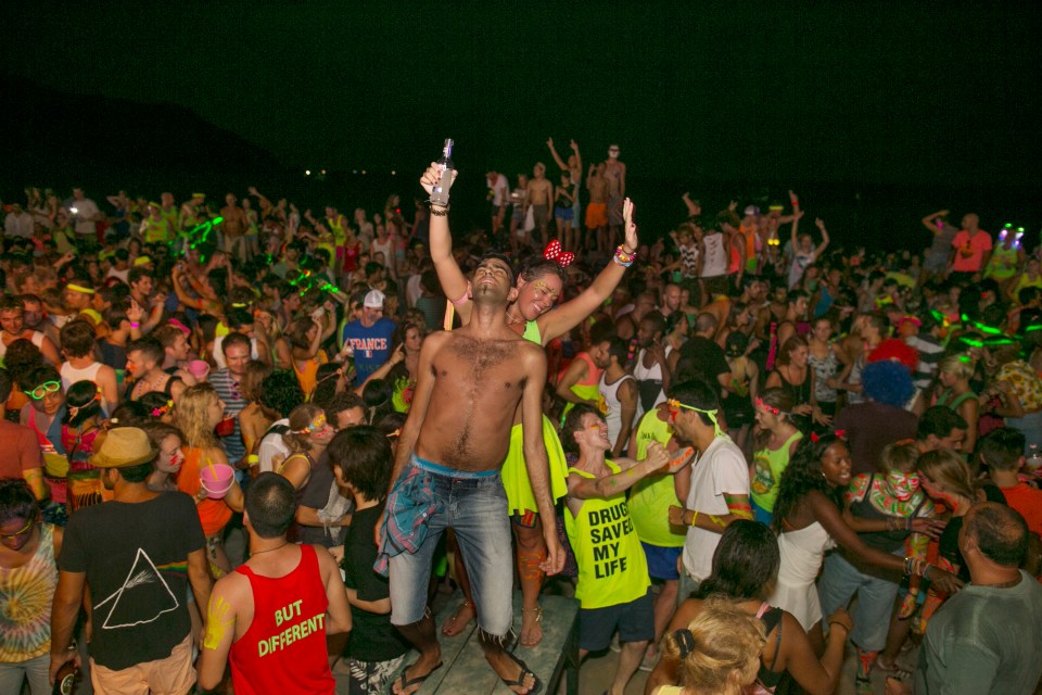 A large group of people dancing at a night beach party.