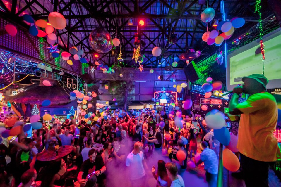 Crowded nightclub with people dancing and balloons floating.