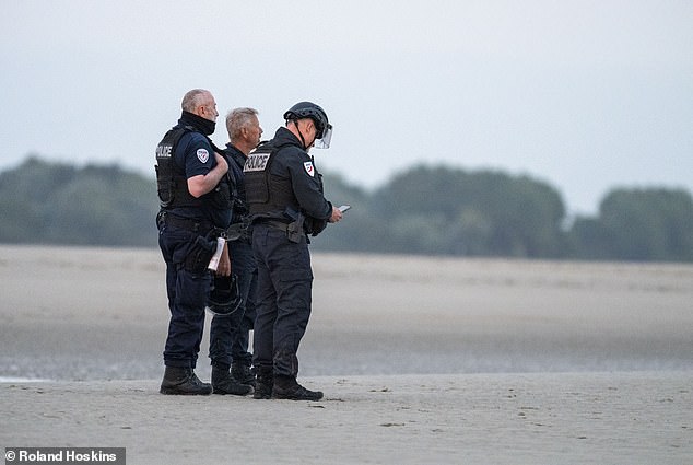 A small group of officers stand stationery as the events unfold. One policeman appears to be looking at his phone (pictured)