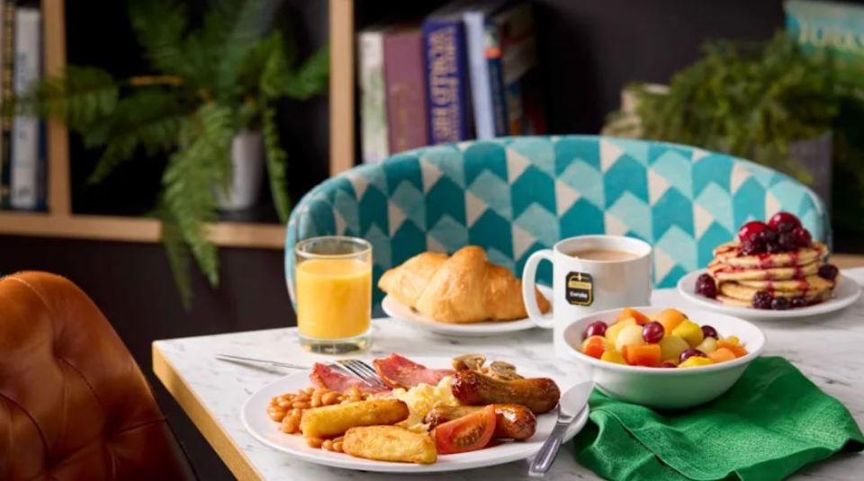 Hotel breakfast spread with full English breakfast, fruit salad, pancakes, croissants, orange juice and tea.