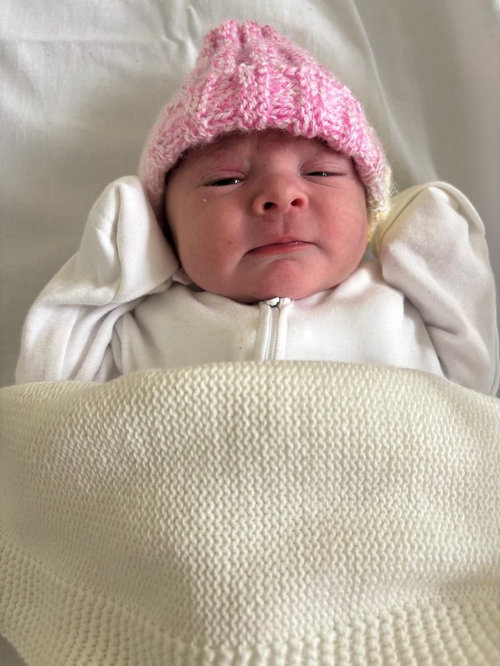 Newborn baby wearing a pink hat and white outfit.
