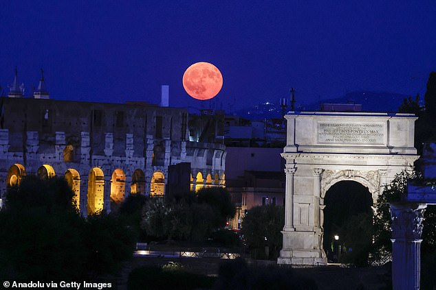 It was captured here rising over the Colosseum and the Arch of Titus at the Roman Forum in Rome, Italy