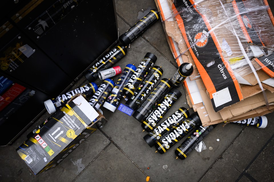 Discarded nitrous oxide canisters and boxes near a bin.
