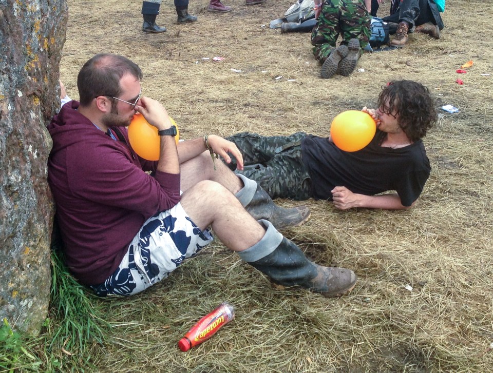 Two men inhaling nitrous oxide from balloons at a music festival.