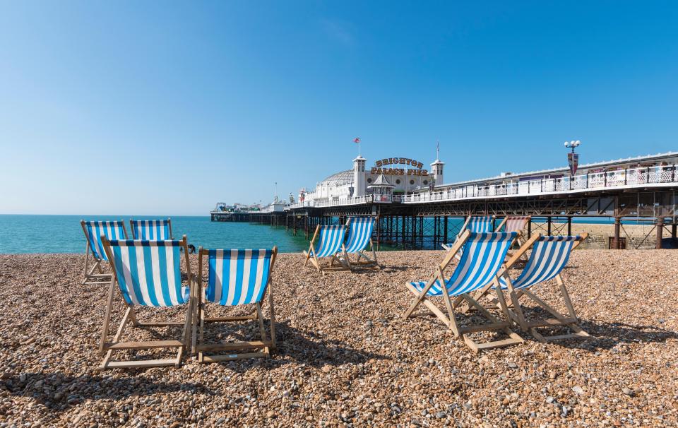 Empty deck chairs on a pebble beach with Brighton Palace Pier in the background.
