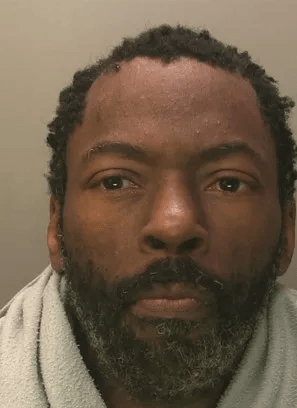 Mugshot of a man with short dreadlocks and a beard.