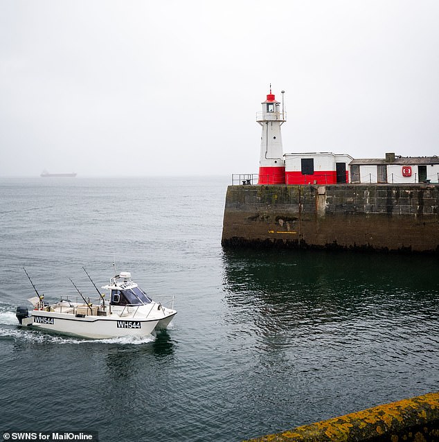 A small vessel comes into the harbour of Newlyn as a container ship looms in the distance