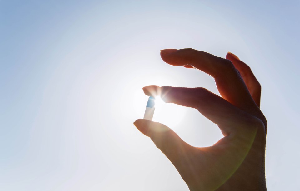Hand holding a pill against the sun.