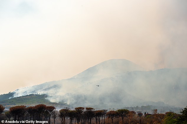 An helicopter flights over flames and smoke rise from a wildfire that breaks out at the Vesuvius National Park in Terzigno, a commune in Naples, Italy on August 9, 2025