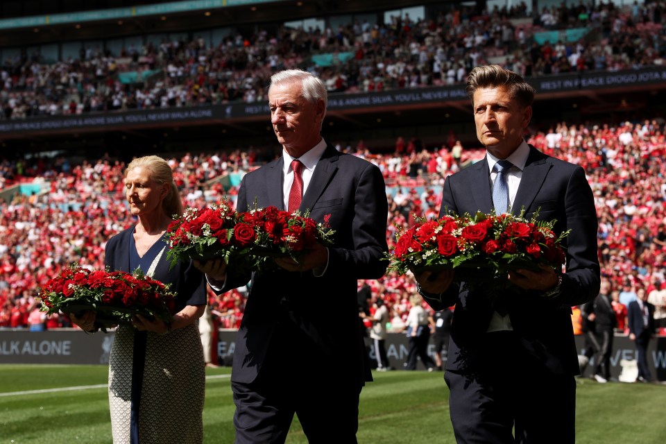 Three people carrying wreaths of red roses at a stadium.
