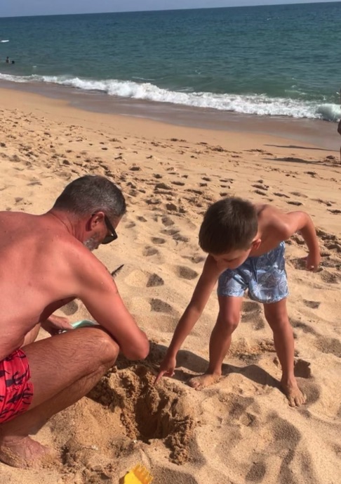 A man and a child digging a hole in the sand at the beach.