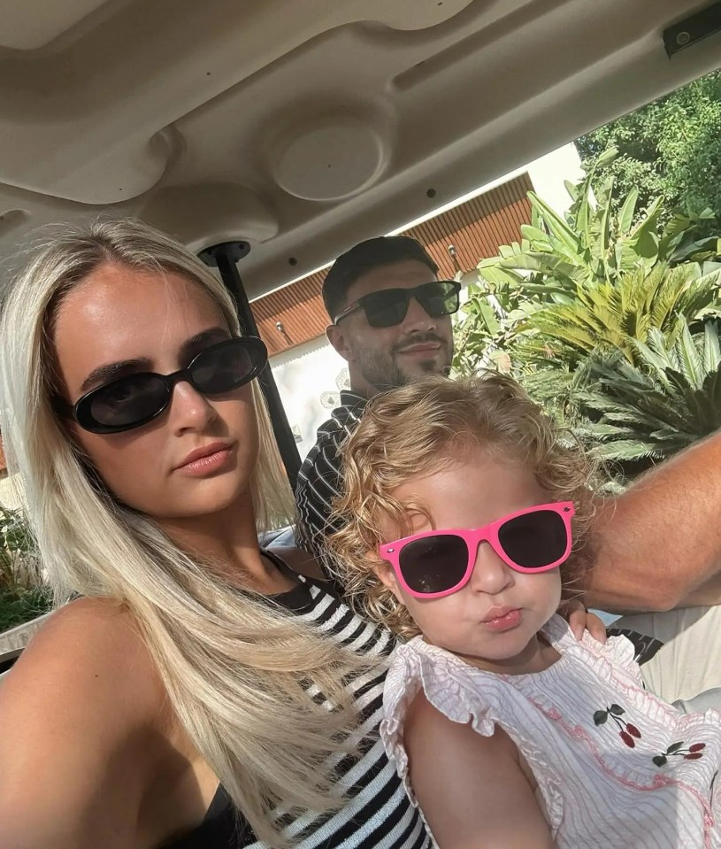 Molly-Mae Hague, a man, and a toddler in sunglasses sitting in a golf cart.