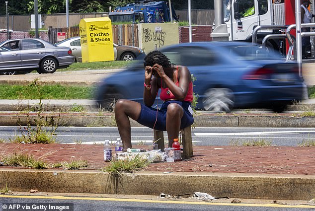 A woman braids her hair at a busy intersection in Washington, DC last month. Trump's executive order makes it easier for cities and states to remove homeless people from the streets and move them to treatment centers