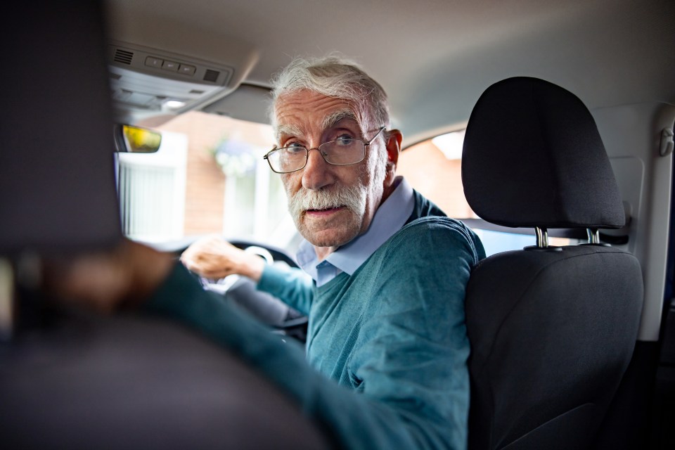 Senior man driving a car and looking over his shoulder.