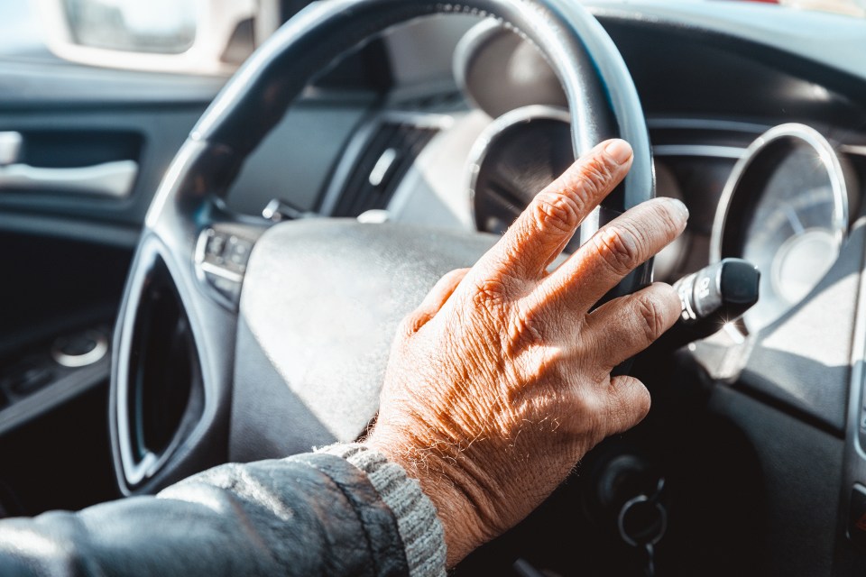 Close-up of a senior man's hand on a car's steering wheel.
