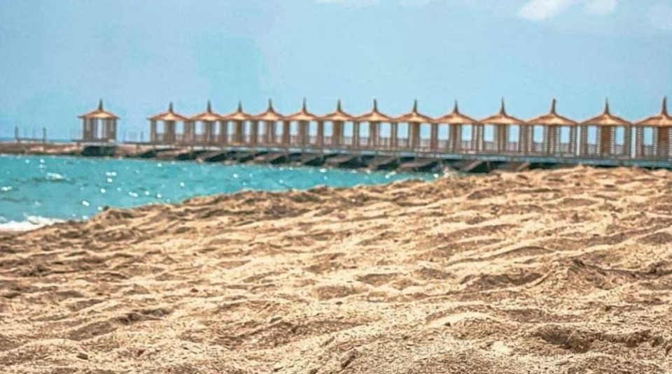 Sandy beach with a row of cabanas over the water.