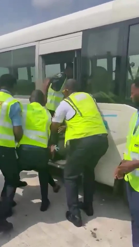 People in yellow safety vests helping someone off a bus.