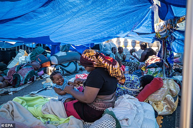Images from the scenes show migrants with blankets and their belongings in plastic shopping bags as they sit under blue tarpaulin sheets