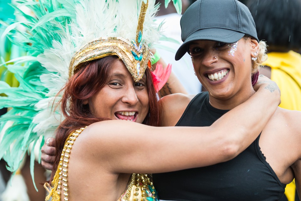 Two women embracing at a carnival. One woman is wearing a feathered headdress.