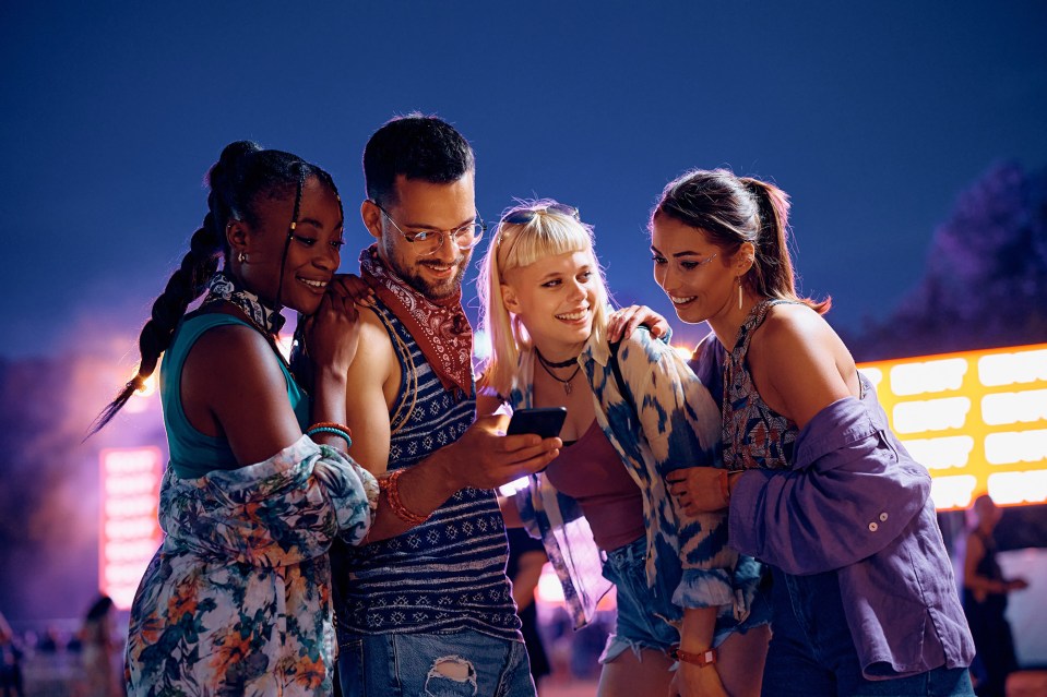 Four friends looking at a smartphone at a music festival.