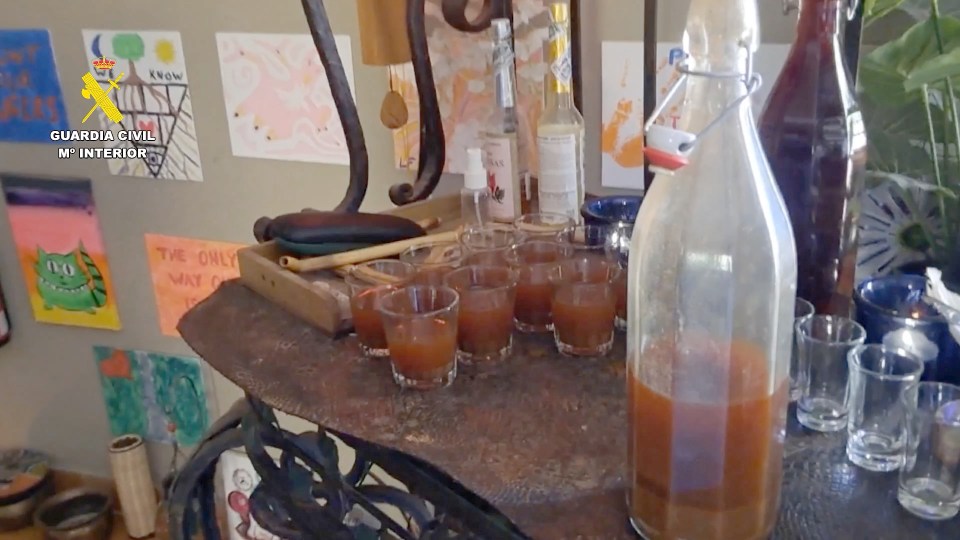 Several shot glasses filled with brown liquid next to a large bottle of the same liquid.