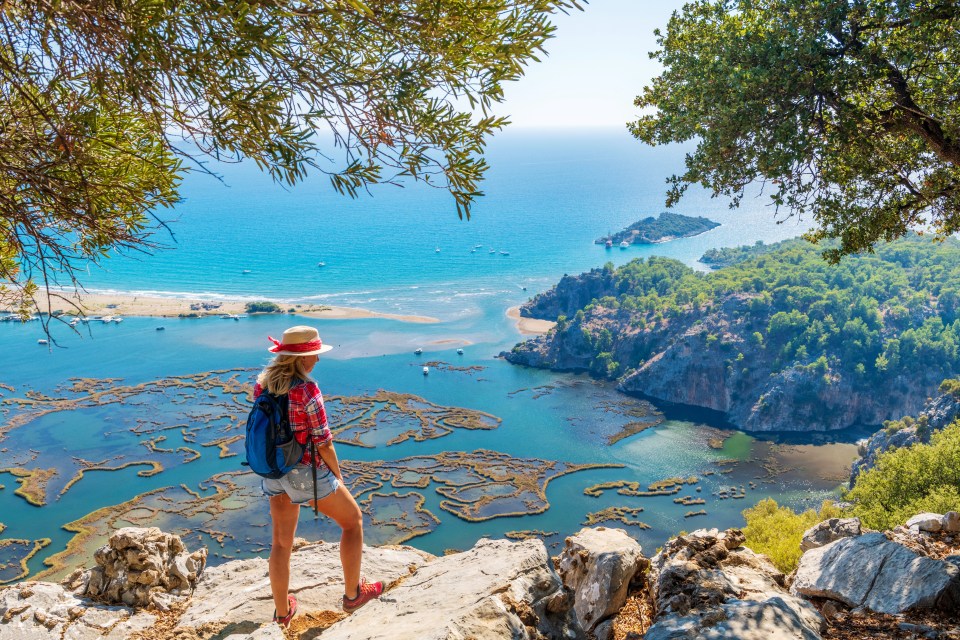 Woman overlooking a beach and ocean from a rocky cliff.