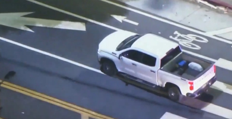 Aerial view of a white truck driving slowly on a city street.