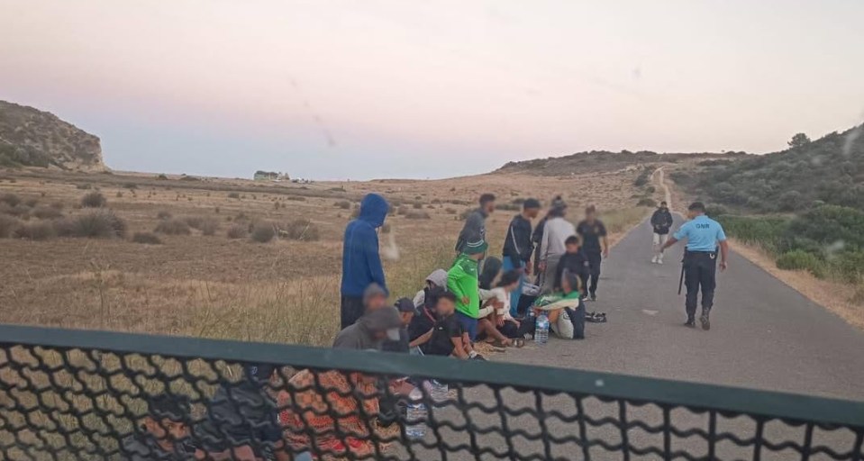 Rescued migrants sitting by the roadside with a GNR officer.