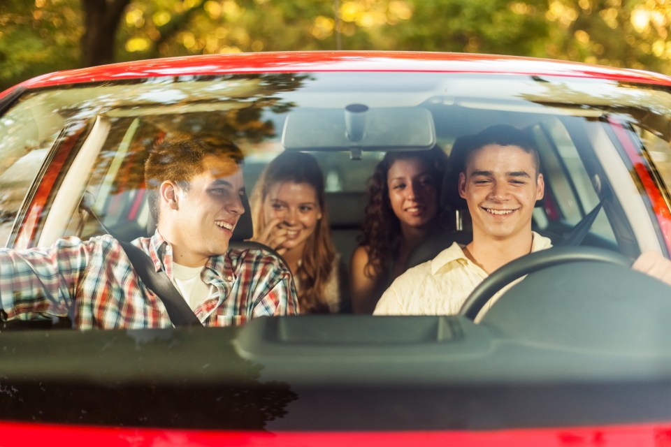 Four young adults smiling in a red car.