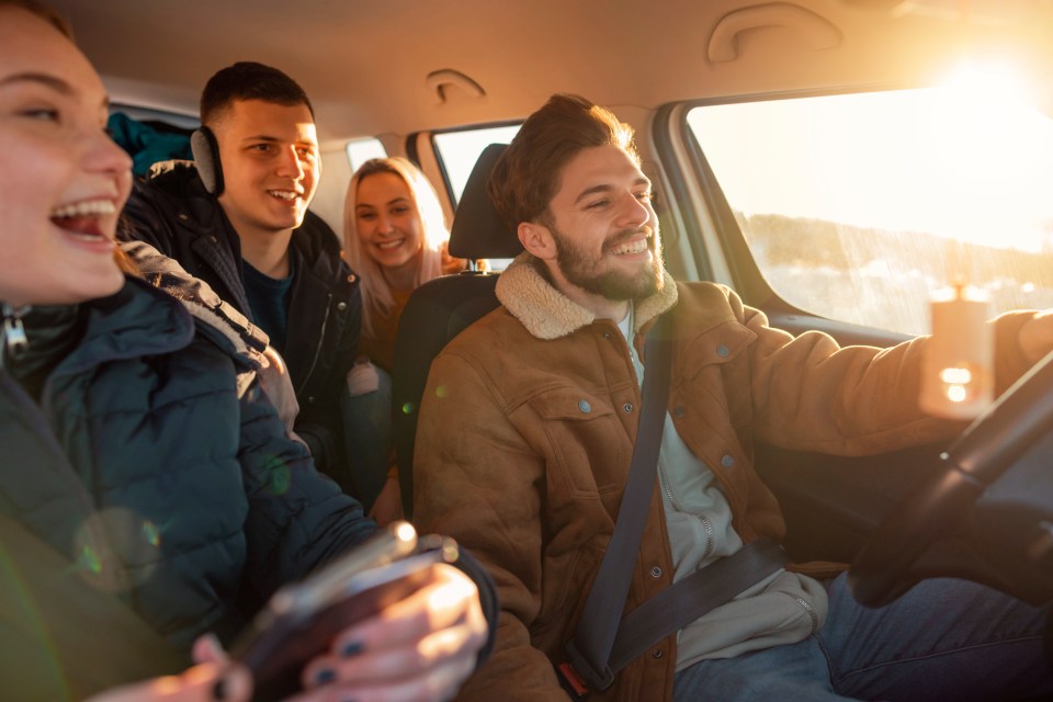 Four young adults smiling in a car on a road trip.