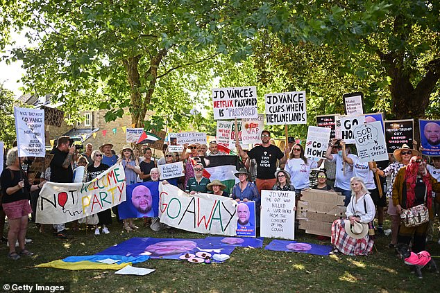 Protestors pose with signs and placards demanding JD Vance return to the US as they campaign against him holidaying in the idyllic village of Chipping Norton