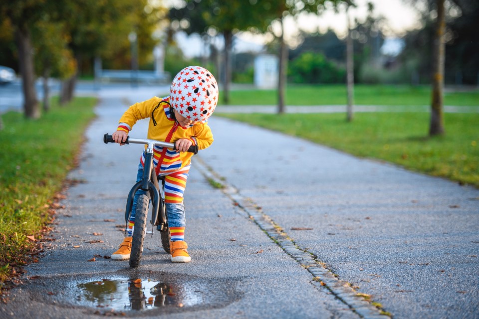 Young boy in helmet riding a balance bike by a puddle.