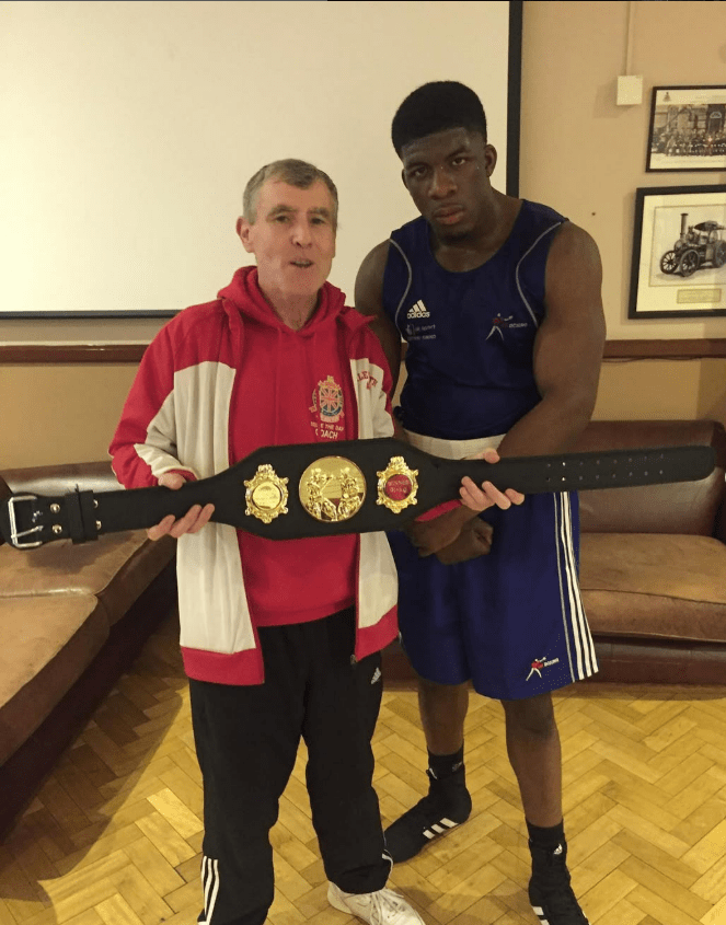 Boxing coach and boxer holding championship belt.