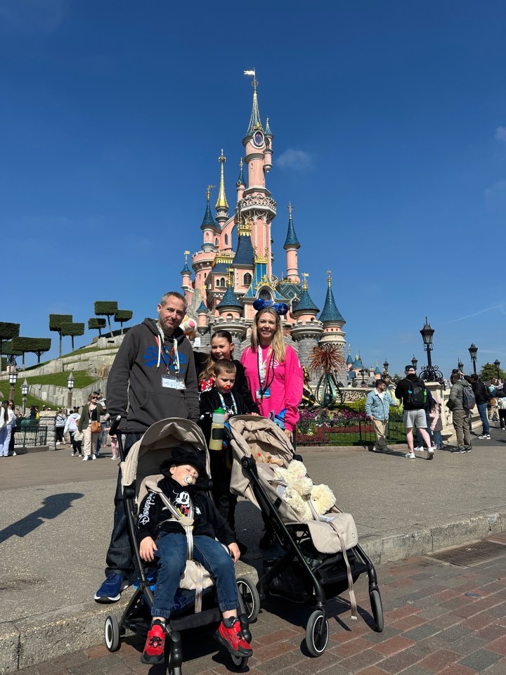 Family with three children posing in front of Sleeping Beauty Castle at Disneyland Paris.