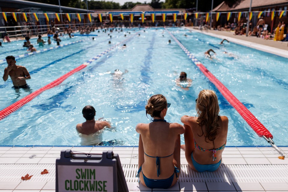 Two women in swimsuits sit by a busy outdoor swimming pool.