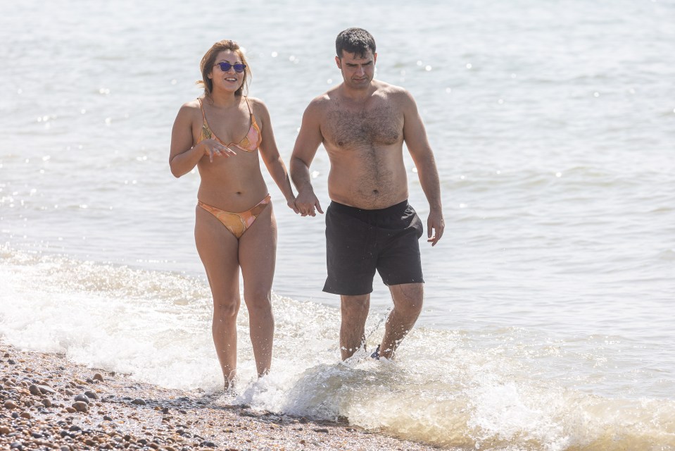 Couple holding hands and walking in the ocean surf on a pebble beach.