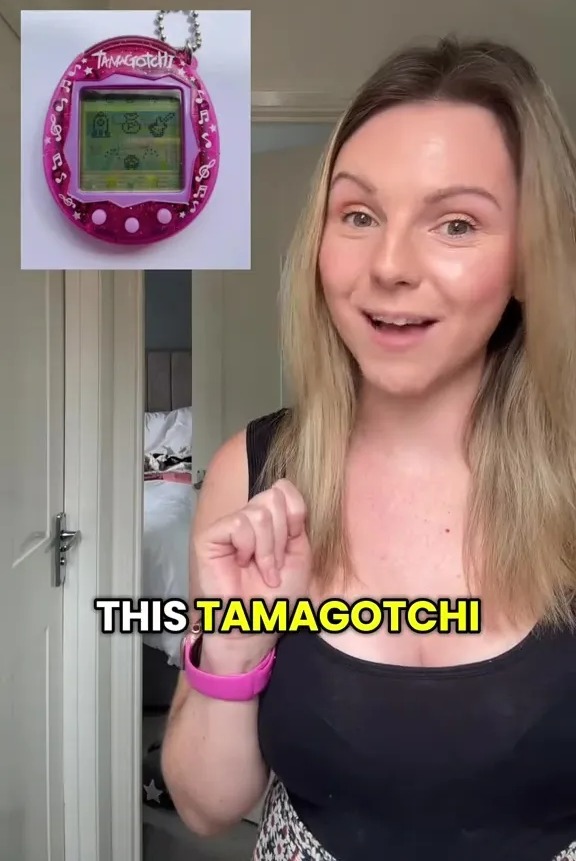 Woman holding up a pink Tamagotchi.