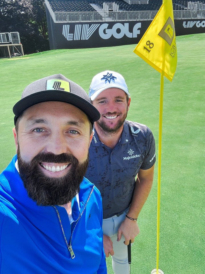 Two men on a golf course, one in a blue shirt and one in a gray shirt.
