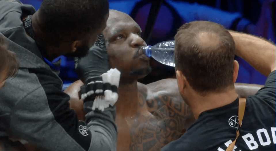 Screenshot of a boxer drinking water while his cornerman cleans his face.