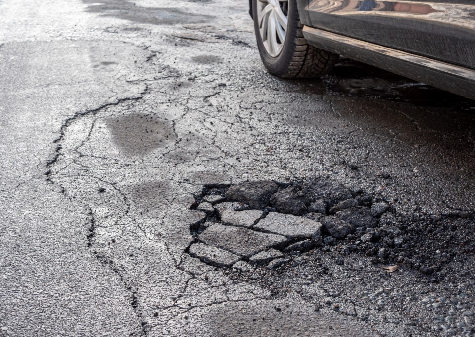 Large pothole in a city street next to a car.