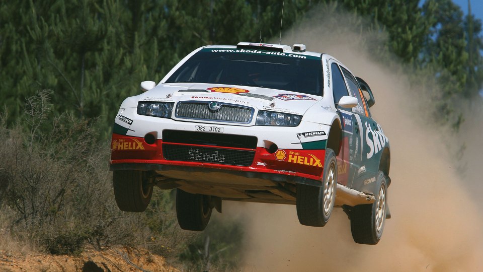 A Skoda rally car airborne over a dirt track.