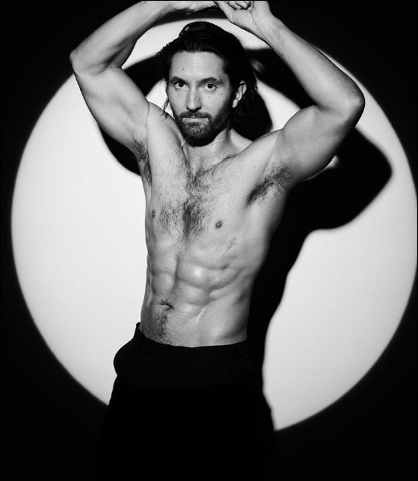 Black and white photo of a shirtless man with his arms raised.