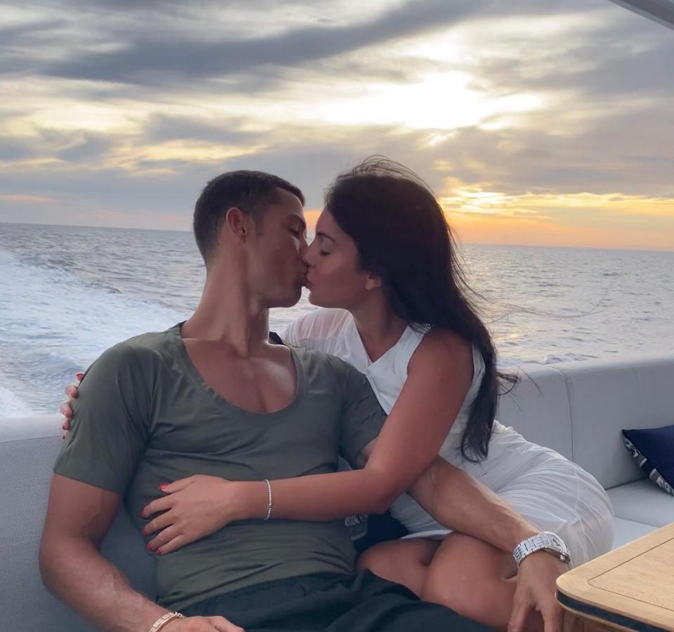 Georgina Rodriguez and Cristiano Ronaldo kissing on a yacht at sunset.
