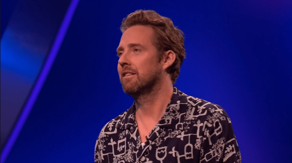 Screenshot of a man speaking in front of a blue background.